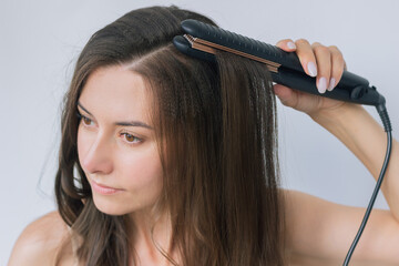close-up of a young pretty Caucasian brunette woman makes herself a basal volume of hair with a...