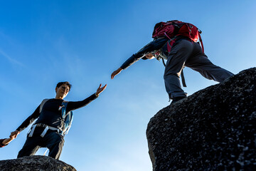 Mountaineer man helping hand to hiker friend during mountaineering on the top of mountain - obrazy, fototapety, plakaty