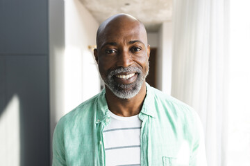 Portrait of happy bald african american mature man with beard smiling in sunny room at home