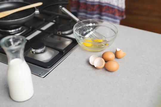 Milk, eggs and mixing bowl with whisk for preparing breakfast on kitchen worktop, copy space