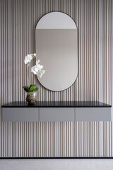 Big oval mirror, table with vase with a flower near wall in modern interior