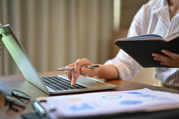 Businesswoman holding her personal daily planner and using laptop at desk