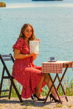 Frau sitzend im Sommer am See und hält eine Kaffeeverpackung in der Hand