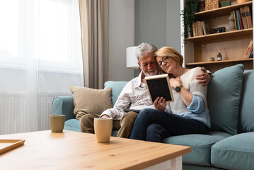 Two elderly people senior couple man and woman looking at a family photo smile and hug while...