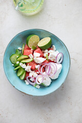 Turquoise bowl with watermelon and feta cheese salad, top view on a light-beige stone background, vertical shot