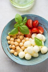 Scamorza cheese, smoked perlini balls, cherry tomatoes and green basil in a turquoise bowl, middle closeup, vertical shot