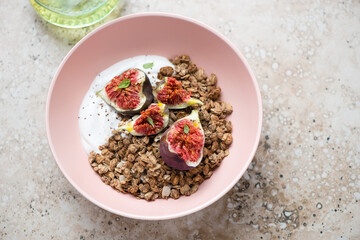 Roseate bowl with granola, greek yogurt and fresh figs, horizontal shot on a beige granite background, elevated view