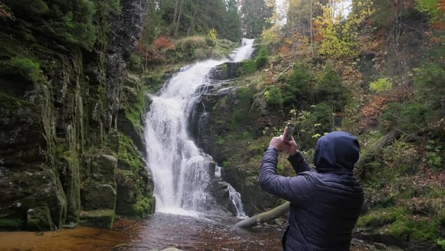 A male tourist takes photos on a smartphone near a waterfall. Vacation