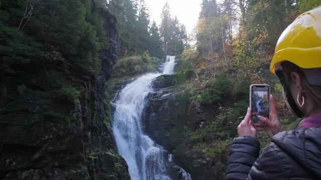 A tourist takes a picture of a waterfall on a smartphone
