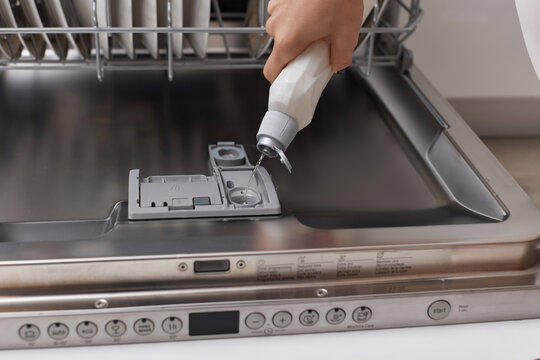 female hand pours rinse aid into the dishwasher compartment in modern white kitchen
