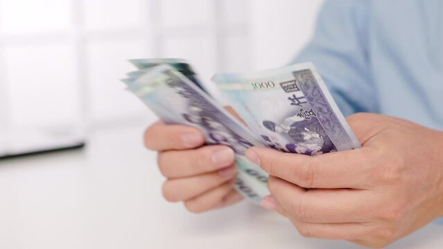 close-up of male hands counting a stack of hundred-dollar Taiwan banknotes.New Taiwan Dollar