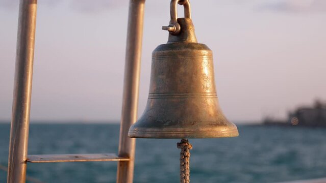 Ship bell in red color on background of blue sky and city of Istanbul, close-up. Hanging from metal arm on background of sea and sky.