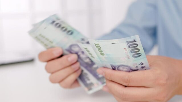 close-up of male hands counting a stack of hundred-dollar Taiwan banknotes.New Taiwan Dollar