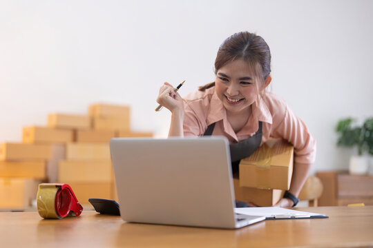 Asian woman entrepreneur prepare parcel box and check online order on laptop computer for commercial checking delivery. online marketing, packing box, SME seller. startup business concept