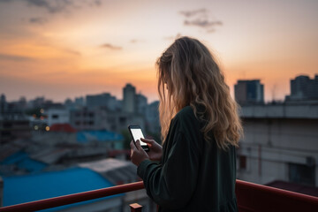 rear view of Woman using mobile phone at rooftop during sunset with copy space, communication or lonely people concept
