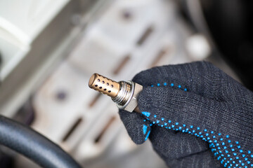 Oxygen sensor for gasoline and diesel engines in the hand against car engine. Mechanic holds oxygen...