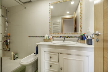 A small bathroom with a built-in cabinet with drawers and white wooden doors, a square mirror...