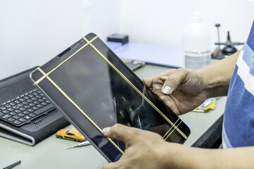 A technician repairing the screen of a large, thin tablet in his electronics workshop