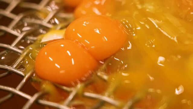 Close up of many egg yolks falling through a small mesh or hole in a factory
