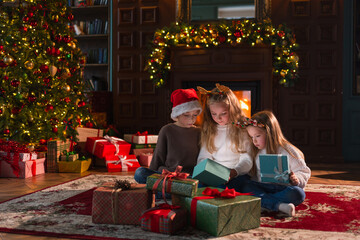 Merry Christmas Xmas holiday. Children unpacking open up gift box near Christmas tree. Kids in...