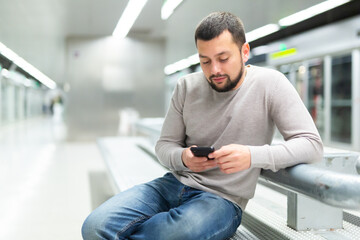 Male passenger in casual clothing reading his mobile phone in subway