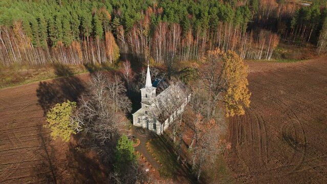 Drone shot, Birds eye view of old, charming countryside church surrounded by fields and forest in autumn