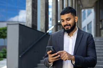 A young Muslim male businessman is using a mobile phone while standing outside an office center....