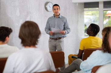 Motivated adult man conducting educational class for interested male group sitting in auditorium