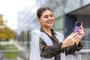 smiling young business woman using mobile phone in front of office building
