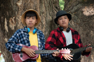 Asian boys are playing acoustic guitar at school park before going to join school summer camp.