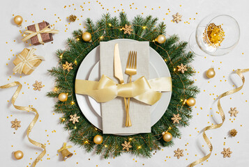 Beautiful Christmas table setting with golden decorations. Plate with gold cutlery in Christmas wreath. New Year party. Top view, flat lay.