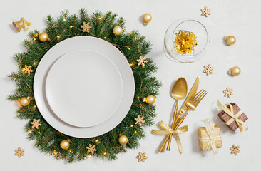 Christmas table setting with empty plate and gold accessories on white background. Plate in a Christmas wreath. New Year party. Top view, flat lay.