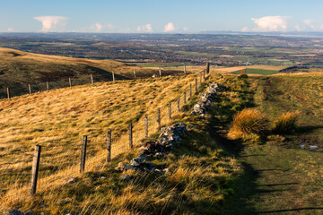 Footpath, trail, through rolling hills of the Scottish Highlands alongside fence in autumn colours