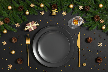 Christmas table setting with black empty plate, gold cutlery and festive decor on black background....