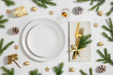 Christmas table setting with empty plate, gold cutlery and festive accessories on white background. New Year party. Top view, flat lay.