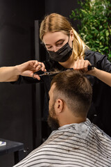 Fototapeta premium Woman hairdresser gives a haircut to a man in a barbershop. Male client looking in the mirror while getting a haircut. Step-by-step haircut. Vertical, Selective Focus, New Life, Male Style