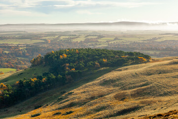 Rolling hills of the Scottish Highlands in colourful autumn with trail and view to fields and towns on light fog