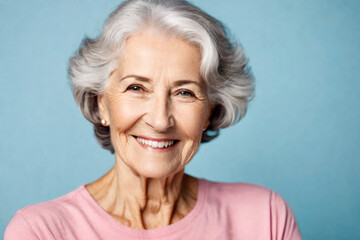Happy beautiful elderly senior model with grey hair in a pink t-shirt on a blue background, portrait of beauty mature old woman with hairstyle and makeup, healthy face skin with wrinkles, dental care