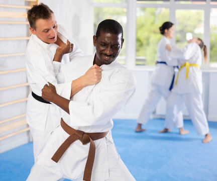 Willing middle-aged man attendee of judo classes doing wrestling in pairs in sports hall