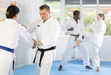 Woman and man in kimono sparring together in gym during karate training