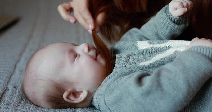 Mother playing with little baby boy touching his face with hair