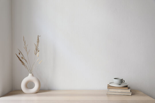 Elegant artistic Scandinavian interior. Modern boho artistic vase. Cup of coffee on old books. Wooden table. Empty wall background. Minimal living room, home office. Decor in cozy apartment.