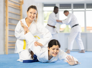 Sportive middle-aged female judo practitioner applying armlock technique on person lying on the...