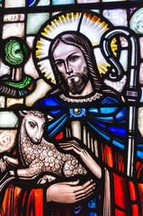 Stained glass window in a church showing Jesus holding a lamb and depicted as a shepherd