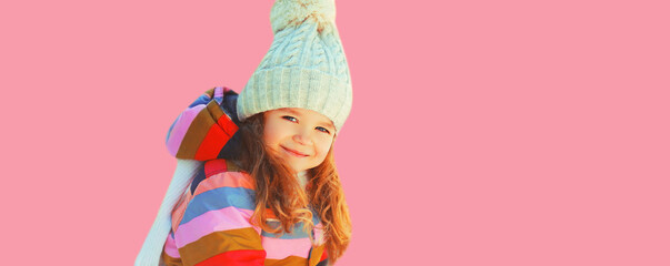 Winter portrait of happy smiling little girl child in jacket and hat on pink background