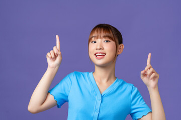 Cute asian woman raise hands up, showing promo, pointing fingers up, stand purple background