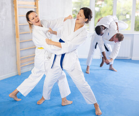 Adult woman and young woman in kimono train judo techniques in group in studio