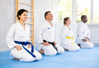Fototapeta na wymiar Group of multiethnic people in kimonos sitting in pose on floor in gym