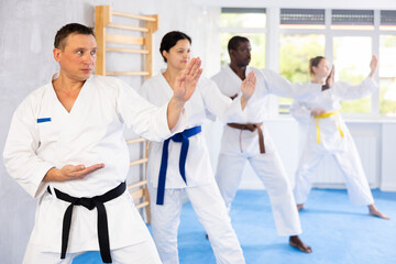 Willing middle-aged guy wearing kimono training karate techniques in group during workout session