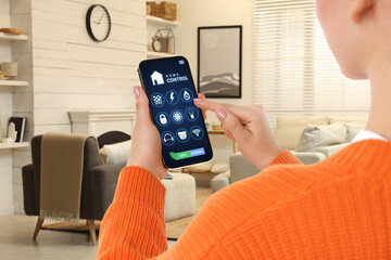 Woman using smart home control system via application on mobile phone indoors, closeup